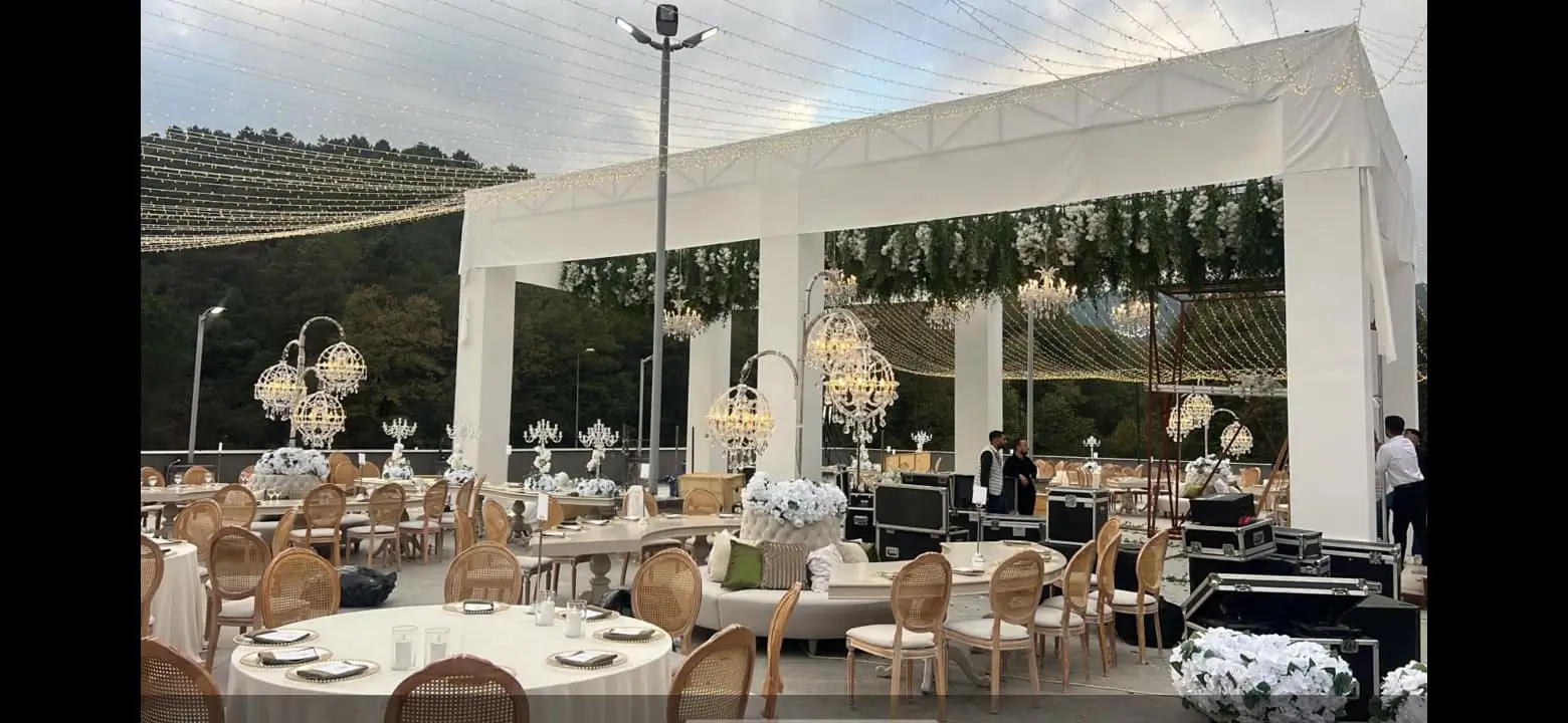 Outdoor banquet installation with dining tables, chairs, production cases and a covered stage area